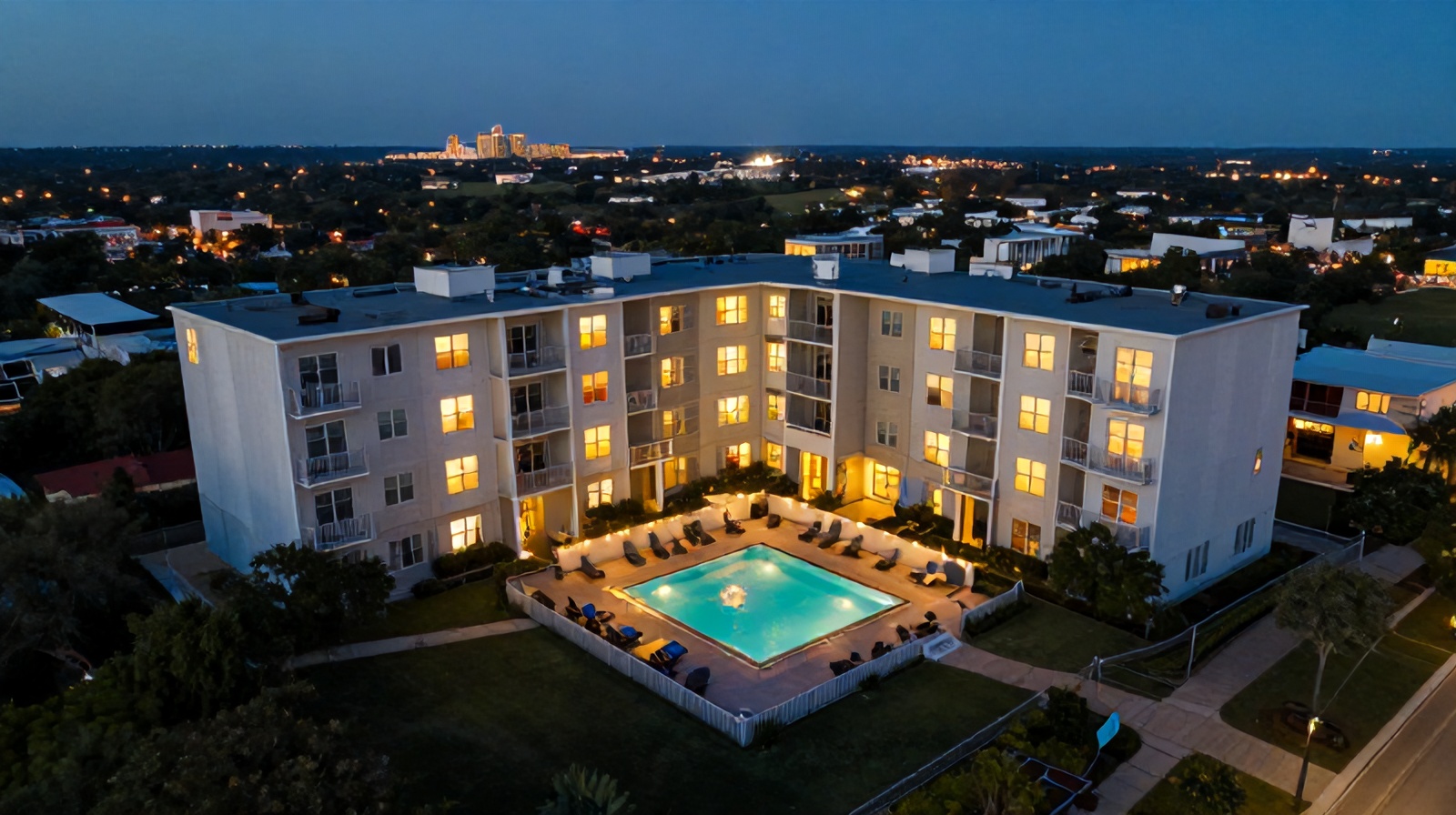 Close aerial view of an illuminated apartment pool deck and building at dusk in Austin
