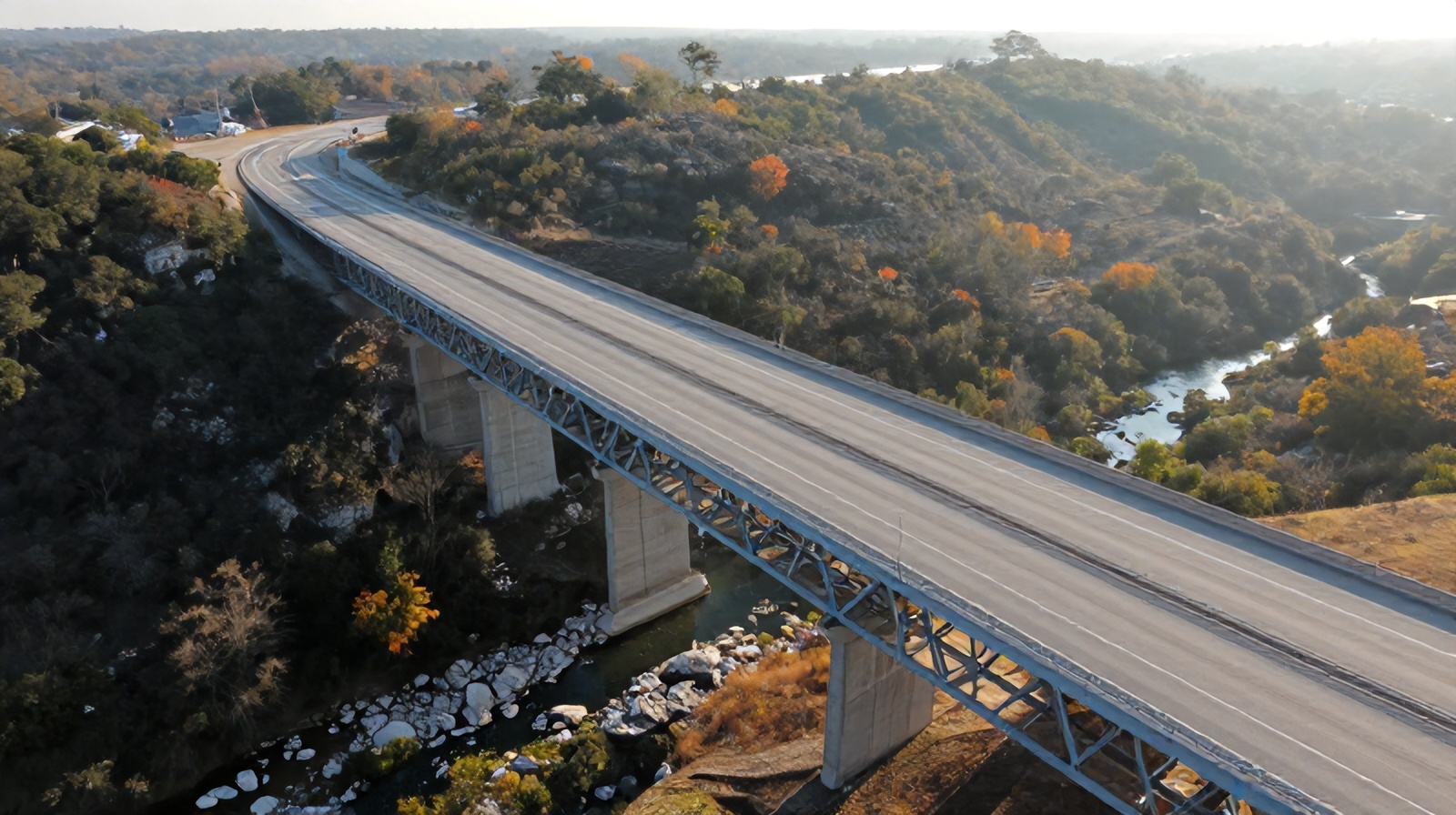 Aerial oblique view of a Central Texas highway bridge spanning a limestone creek at sunrise