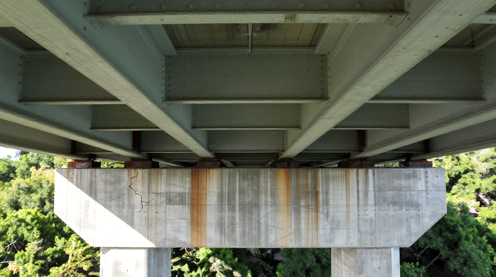 Close-up aerial view beneath a bridge showing girders, pier caps, and structural wear details
