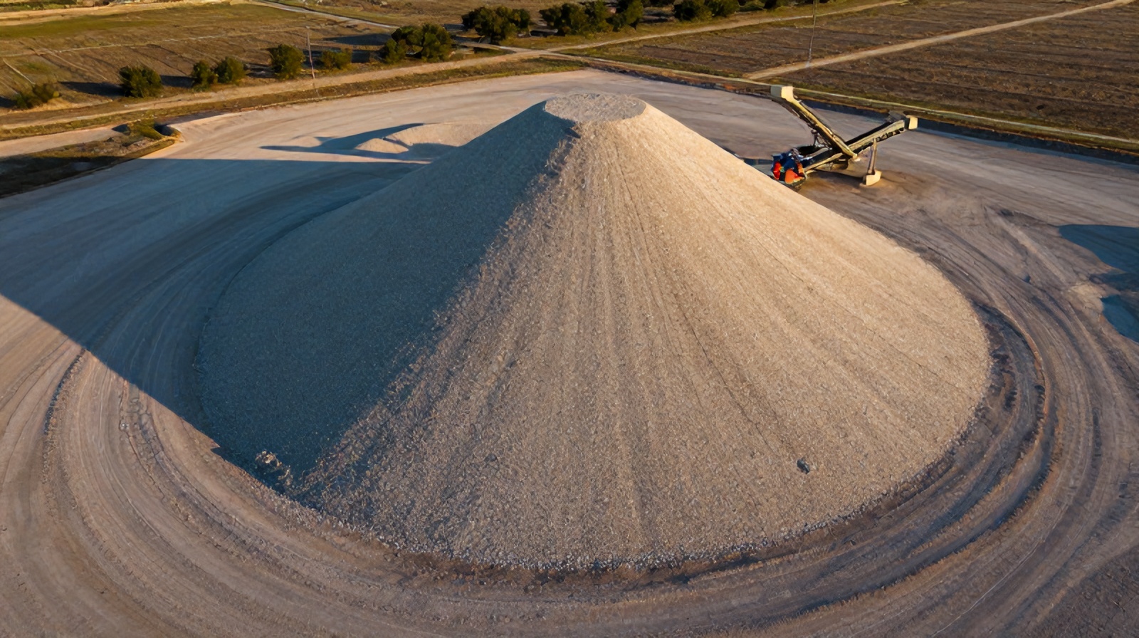Oblique aerial close-up of a conical crushed-stone stockpile with a conveyor stacker
