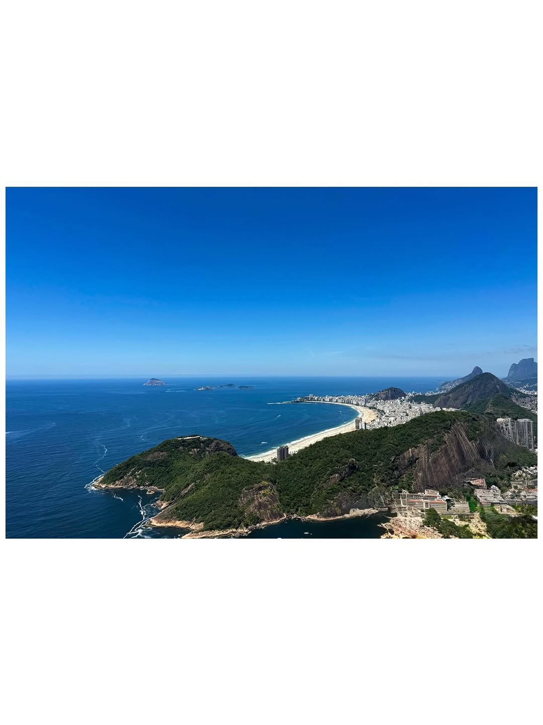 Coastal Views - Aerial photograph of a curved beach and rocky coastline with mountains in the background