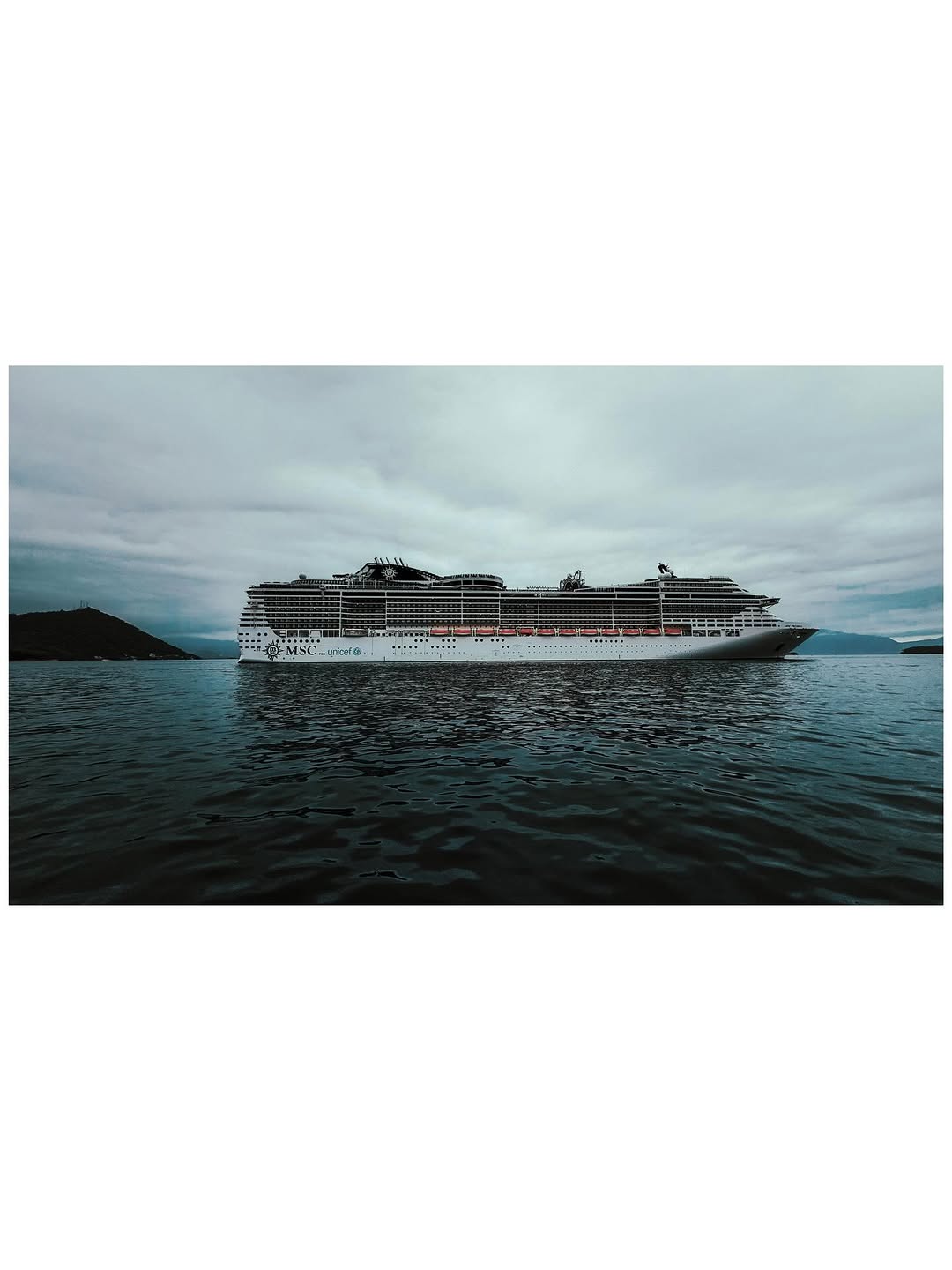 Commercial Spot - MSC cruise ship sailing through calm waters with mountainous coastline under dramatic overcast skies