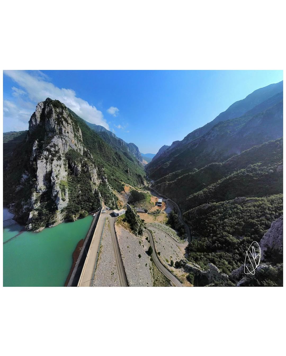 Mountain Expedition - Aerial drone view of a dramatic mountain valley with turquoise reservoir, dam, and winding road through rugged peaks
